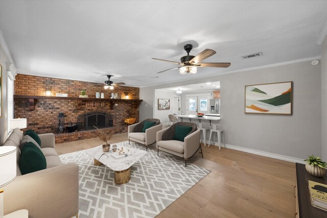 unfurnished living room featuring light hardwood / wood-style floors, brick wall, a brick fireplace, crown molding, and ceiling fan