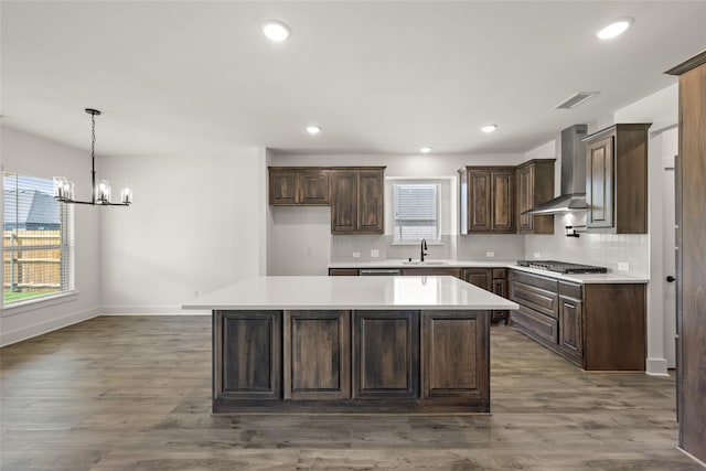 kitchen with a center island, wall chimney exhaust hood, sink, dark hardwood / wood-style flooring, and stainless steel gas cooktop