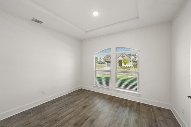 spare room with a tray ceiling, dark wood finished floors, baseboards, visible vents, and crown molding