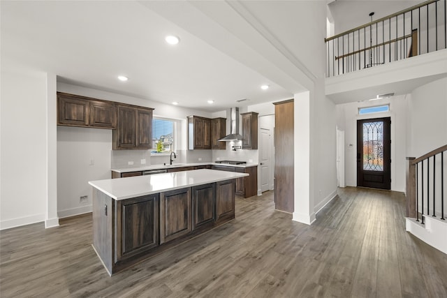 kitchen with a center island, wall chimney exhaust hood, sink, dark hardwood / wood-style flooring, and stainless steel gas stovetop