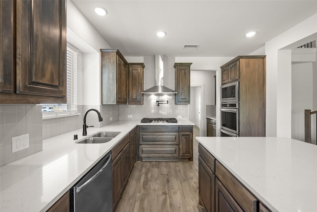 kitchen featuring wall chimney range hood, light hardwood / wood-style floors, tasteful backsplash, sink, and stainless steel appliances