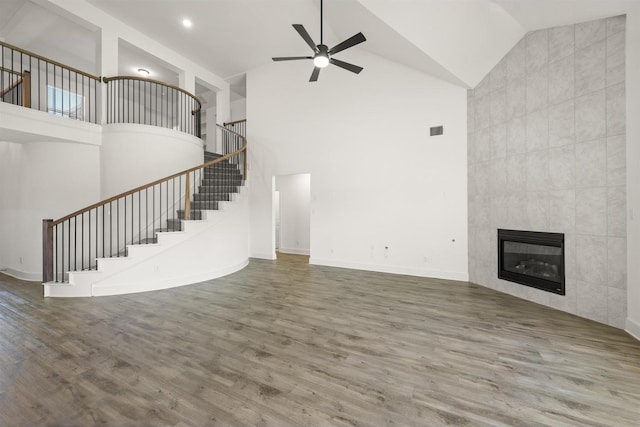 unfurnished living room featuring ceiling fan, wood finished floors, high vaulted ceiling, and stairway