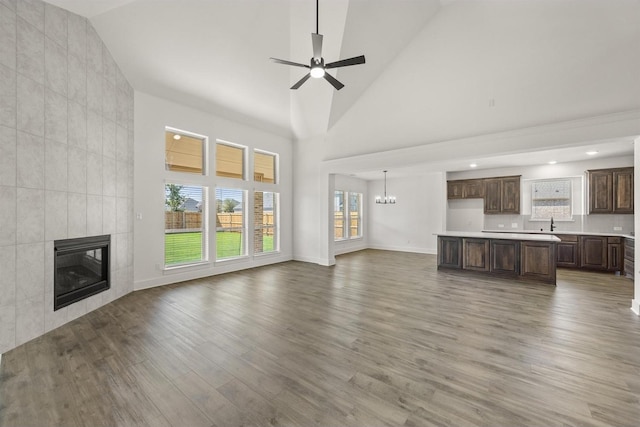 unfurnished living room with high vaulted ceiling, ceiling fan with notable chandelier, light wood-type flooring, a fireplace, and baseboards