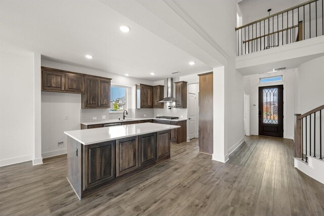 kitchen featuring a sink, stainless steel gas stovetop, light countertops, wall chimney exhaust hood, and baseboards