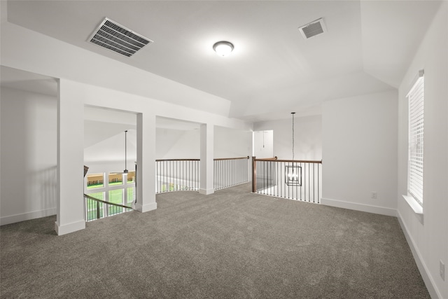 empty room with dark colored carpet, an inviting chandelier, and vaulted ceiling