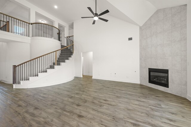 unfurnished living room featuring stairway, wood finished floors, a ceiling fan, a fireplace, and high vaulted ceiling