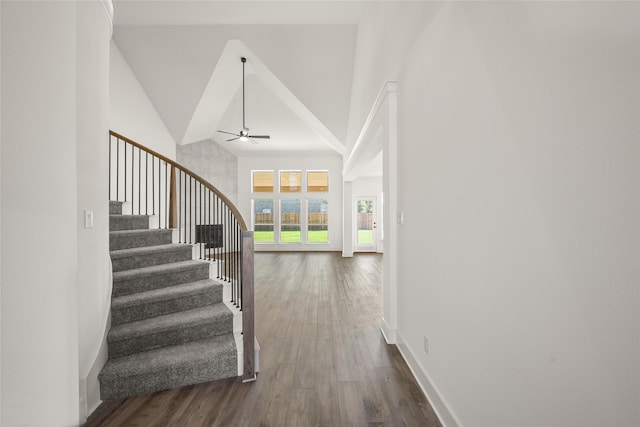 stairway with ceiling fan, wood-type flooring, and high vaulted ceiling