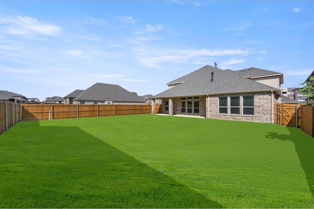 rear view of house featuring a fenced backyard, brick siding, a shingled roof, and a lawn