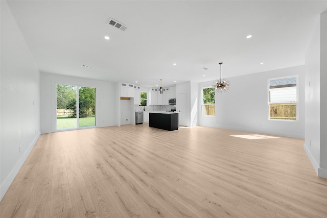 unfurnished living room with light hardwood / wood-style flooring, a notable chandelier, and plenty of natural light