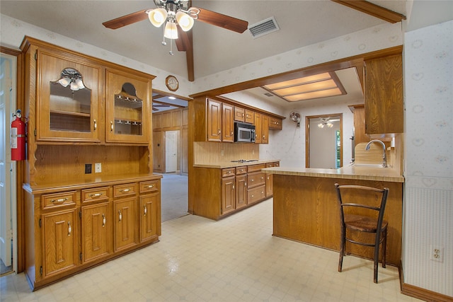 kitchen with kitchen peninsula, ceiling fan, sink, beam ceiling, and a breakfast bar