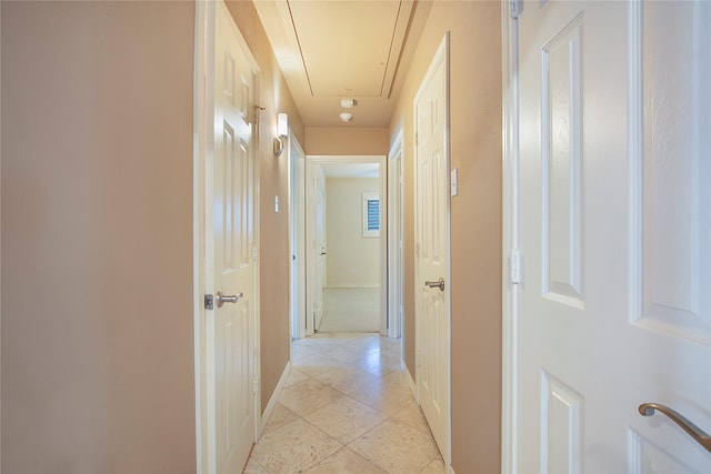 corridor featuring light tile patterned floors, attic access, and baseboards