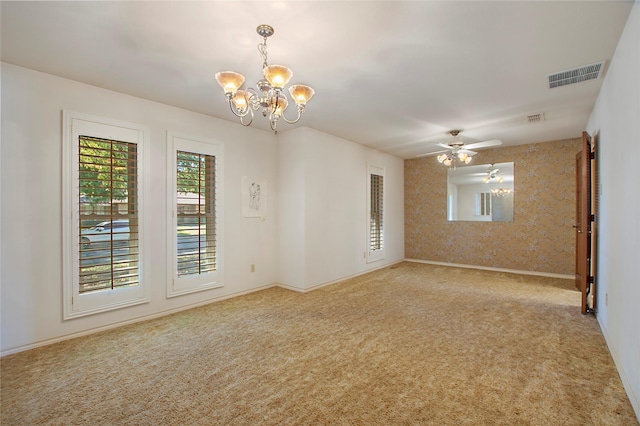 carpeted spare room featuring ceiling fan with notable chandelier