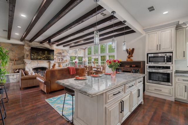 kitchen featuring appliances with stainless steel finishes, light stone counters, beamed ceiling, a center island, and dark hardwood / wood-style floors