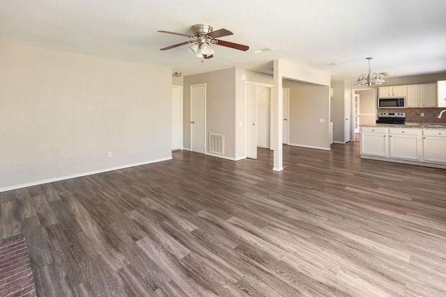 unfurnished living room with a sink, dark wood-style flooring, baseboards, visible vents, and ceiling fan with notable chandelier