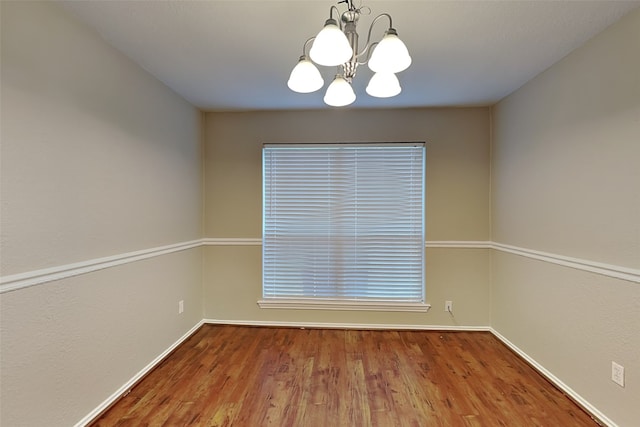 spare room featuring wood-type flooring and a chandelier