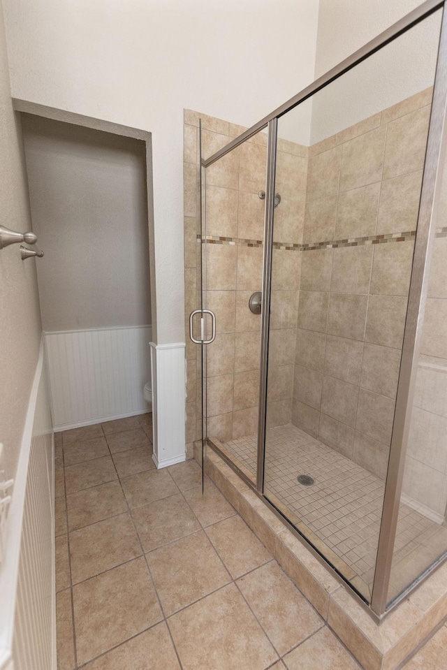 bathroom featuring tile patterned floors, toilet, a stall shower, and wainscoting