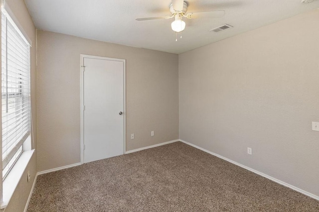 unfurnished room with carpet floors, visible vents, a ceiling fan, and baseboards