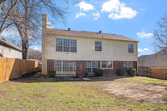 rear view of house with a lawn, a fenced backyard, a chimney, and brick siding