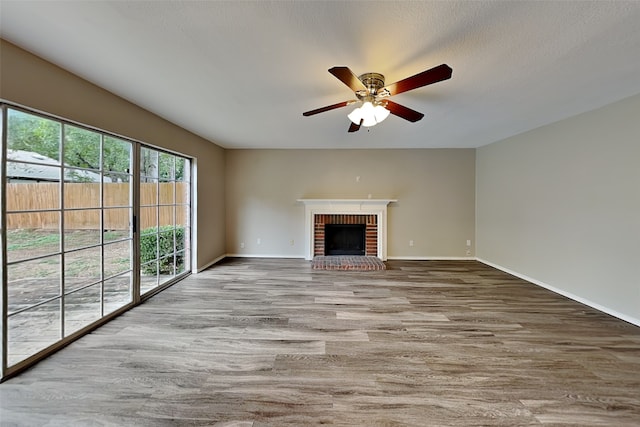 unfurnished living room featuring a textured ceiling, hardwood / wood-style flooring, a brick fireplace, and ceiling fan