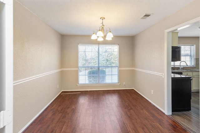 unfurnished dining area with wood-type flooring, baseboards, a notable chandelier, and visible vents
