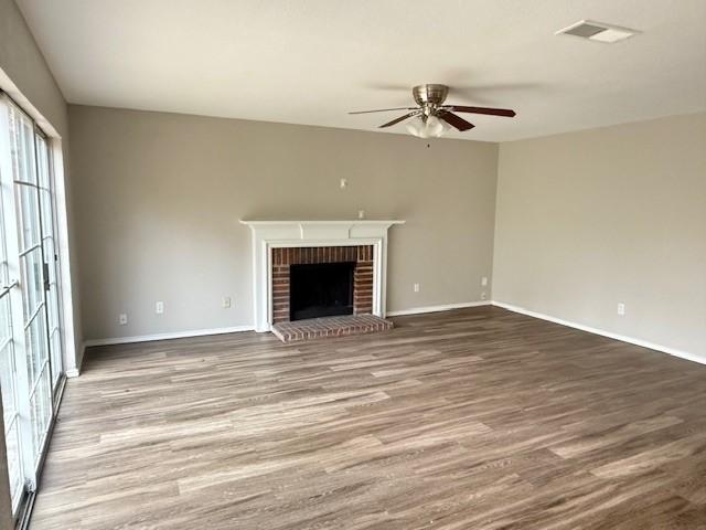 unfurnished living room featuring hardwood / wood-style floors, a brick fireplace, and ceiling fan