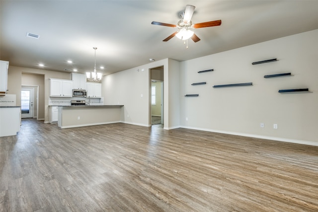 unfurnished living room with ceiling fan with notable chandelier and light wood-type flooring