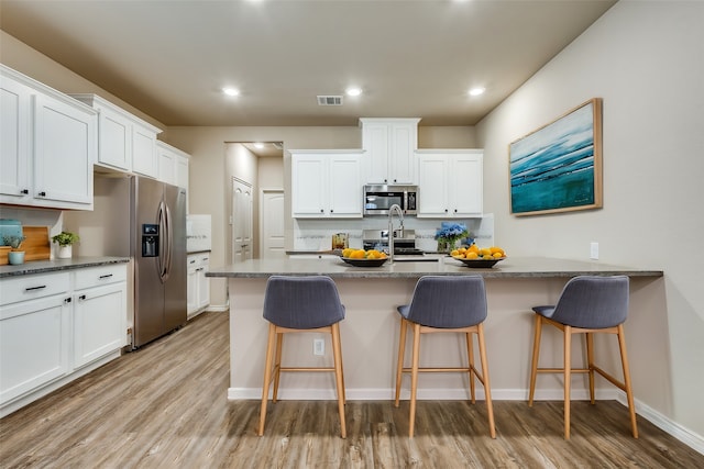 kitchen with white cabinets, stainless steel appliances, a kitchen bar, and light hardwood / wood-style flooring