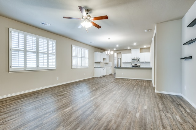 unfurnished living room featuring wood-type flooring and ceiling fan with notable chandelier