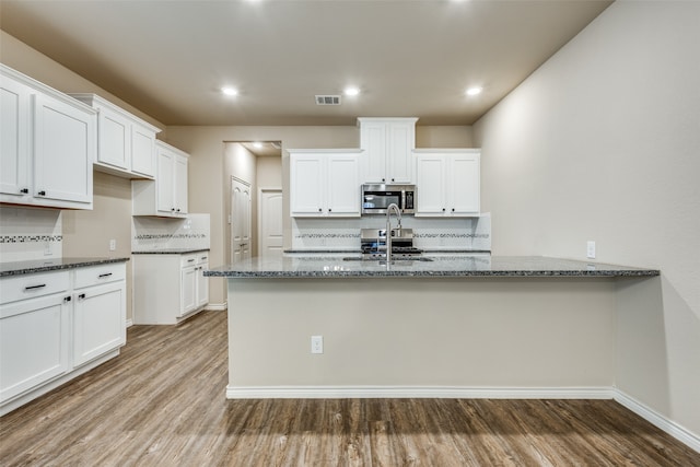 kitchen with white cabinets, light hardwood / wood-style flooring, backsplash, and dark stone counters