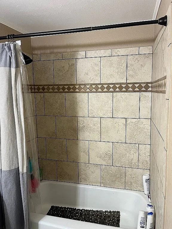 bathroom with a textured ceiling and shower / tub combo with curtain