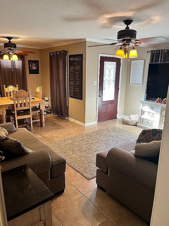 tiled living room featuring ceiling fan, a textured ceiling, and ornamental molding