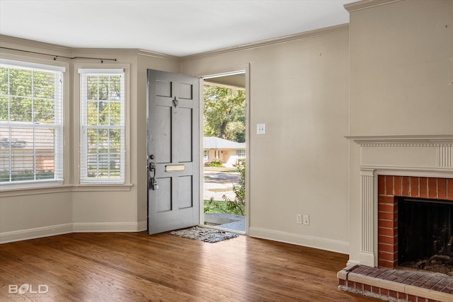 foyer entrance featuring wood-type flooring, crown molding, and a brick fireplace