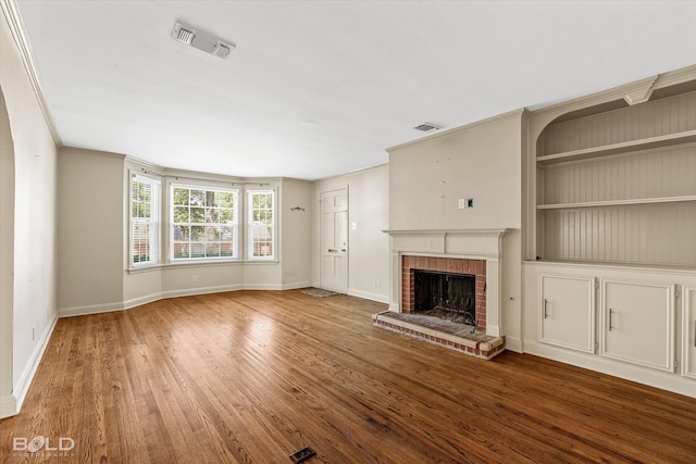 unfurnished living room with a brick fireplace, wood-type flooring, and crown molding