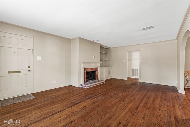 unfurnished living room featuring dark hardwood / wood-style flooring, built in features, ornamental molding, and a brick fireplace