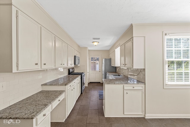 kitchen with white cabinets, appliances with stainless steel finishes, sink, and light stone countertops