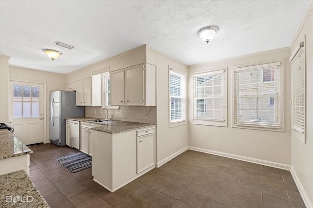 kitchen with light stone counters, backsplash, appliances with stainless steel finishes, sink, and white cabinets