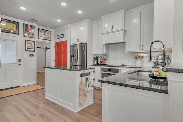 kitchen with decorative backsplash, light hardwood / wood-style flooring, stainless steel appliances, a barn door, and white cabinets