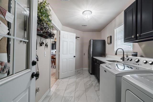 clothes washing area with a notable chandelier, cabinets, sink, and washer and dryer