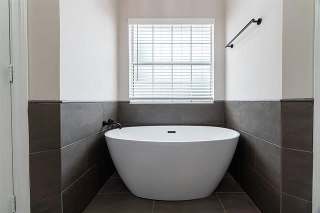 bathroom with tile walls, a washtub, and tile patterned floors