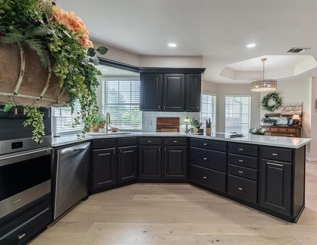 kitchen featuring appliances with stainless steel finishes, pendant lighting, light wood-type flooring, a tray ceiling, and sink