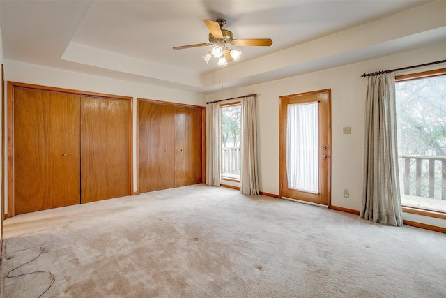 unfurnished bedroom with ceiling fan, light carpet, two closets, and a tray ceiling