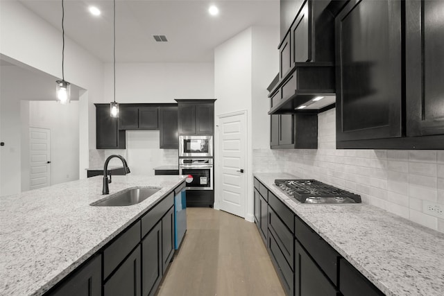 kitchen with hardwood / wood-style floors, sink, light stone counters, stainless steel appliances, and hanging light fixtures