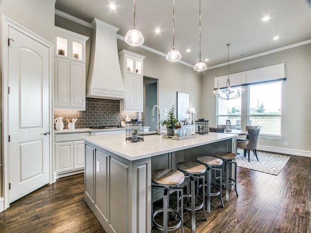 kitchen with pendant lighting, dark hardwood / wood-style flooring, a center island with sink, premium range hood, and white cabinetry