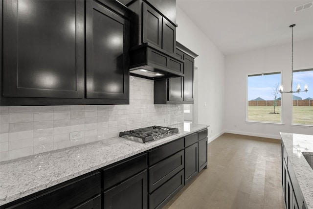 kitchen featuring light stone counters, stainless steel gas stovetop, decorative backsplash, and decorative light fixtures