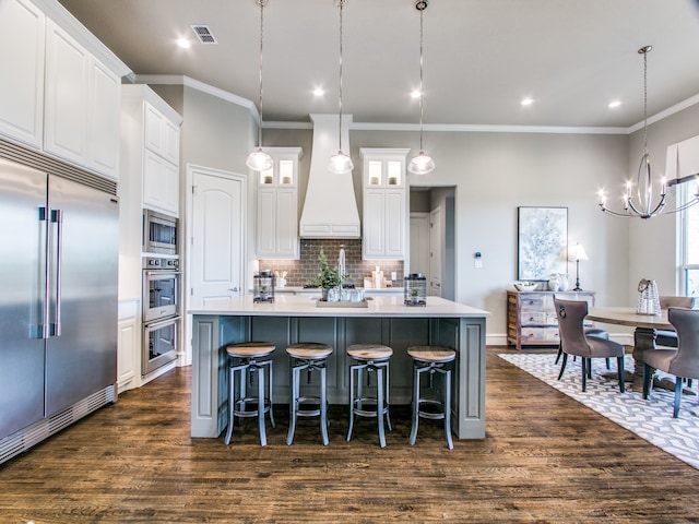 kitchen with a large island with sink, built in appliances, dark hardwood / wood-style floors, premium range hood, and white cabinetry