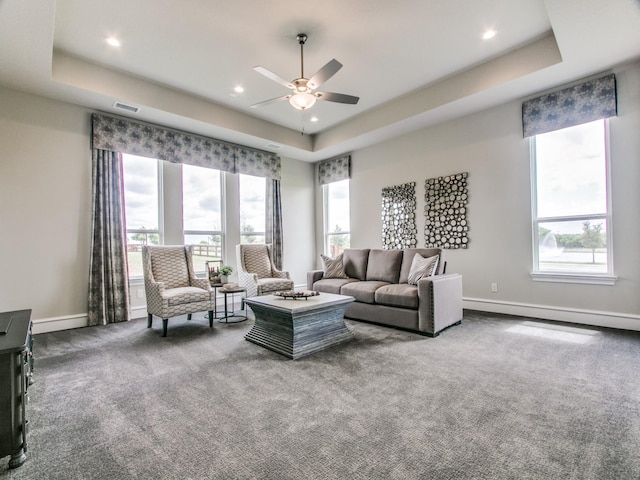 carpeted living room with a baseboard heating unit, ceiling fan, and a raised ceiling