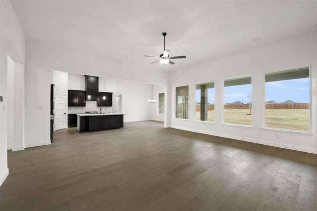 unfurnished living room featuring ceiling fan with notable chandelier and dark hardwood / wood-style flooring