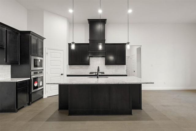 kitchen featuring stainless steel oven, light stone countertops, a kitchen island with sink, and decorative light fixtures