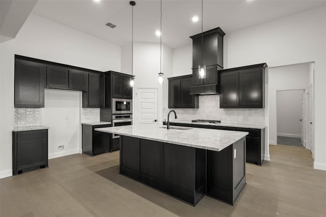 kitchen featuring hanging light fixtures, stainless steel appliances, a towering ceiling, sink, and a kitchen island with sink