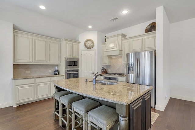 kitchen featuring sink, an island with sink, stainless steel appliances, backsplash, and dark hardwood / wood-style flooring